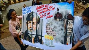 Protesters holding a poster demanding extradition of 26/11 mastermind Tahawwur Rana, featuring his sketch behind bars and visuals of the Mumbai attacks.